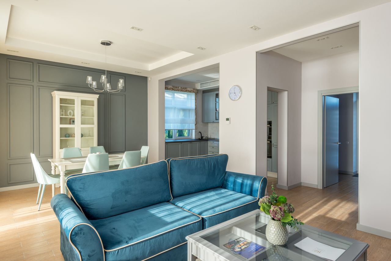 Bright modern living room featuring blue sofa, dining table, and elegant decor.